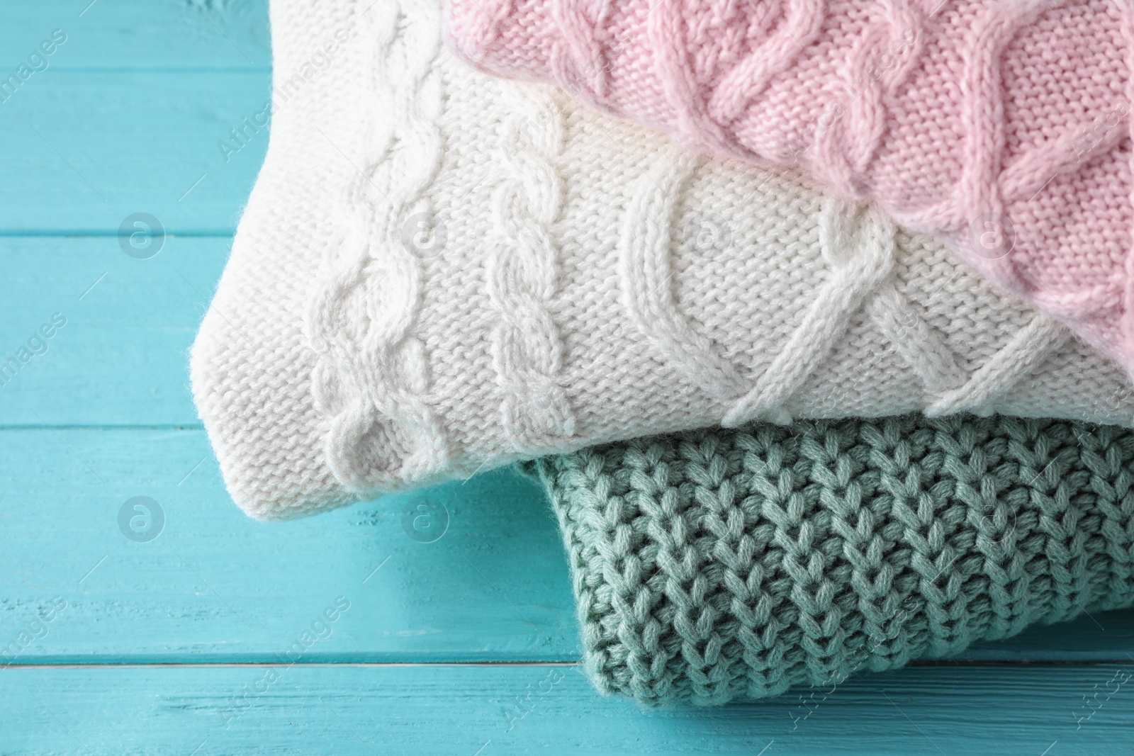 Image of Stack of folded warm sweaters on turquoise wooden background, closeup