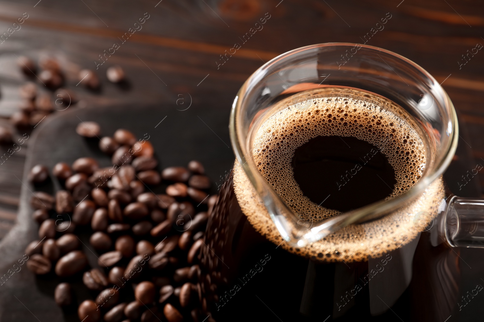 Photo of Glass turkish coffee pot with hot drink and beans on wooden table, closeup. Space for text