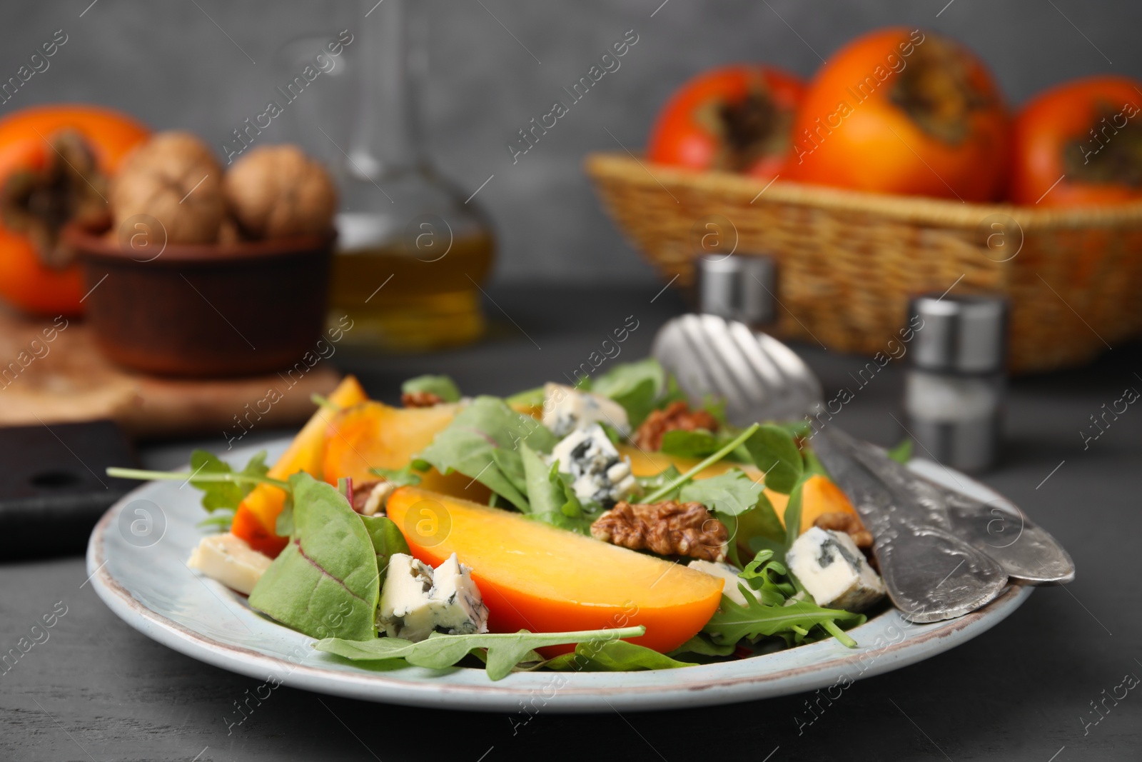 Photo of Tasty salad with persimmon, blue cheese and walnuts served on grey wooden table, closeup