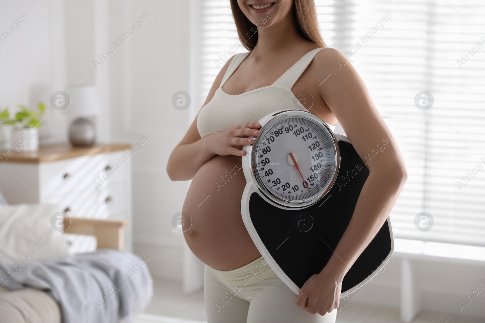 Photo of Young pregnant woman with scales at home, closeup