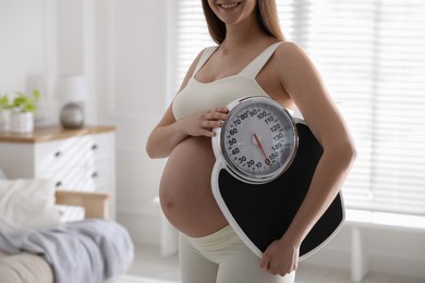 Photo of Young pregnant woman with scales at home, closeup
