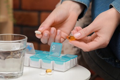 Photo of Woman taking pills from plastic box at white table indoors, closeup