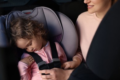 Mother fastening her sleeping daughter in child safety seat inside car