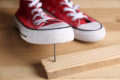 Metal nail in wooden plank and shoes on table, closeup