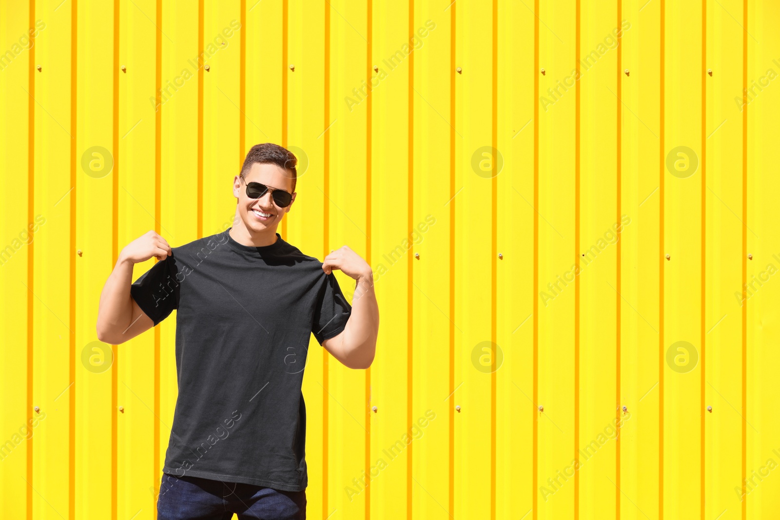 Photo of Young man in black t-shirt near color wall. Mockup for design