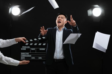 Photo of Emotional asian actor performing role while second assistant camera holding clapperboard on stage. Film industry