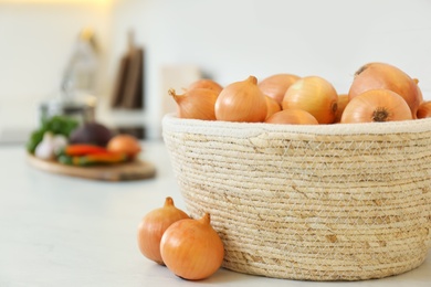 Photo of Fresh onions in wicker basket on white countertop, closeup