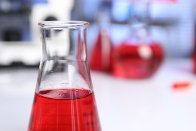 Laboratory analysis. Glass flask with red liquid on white table indoors, closeup. Space for text