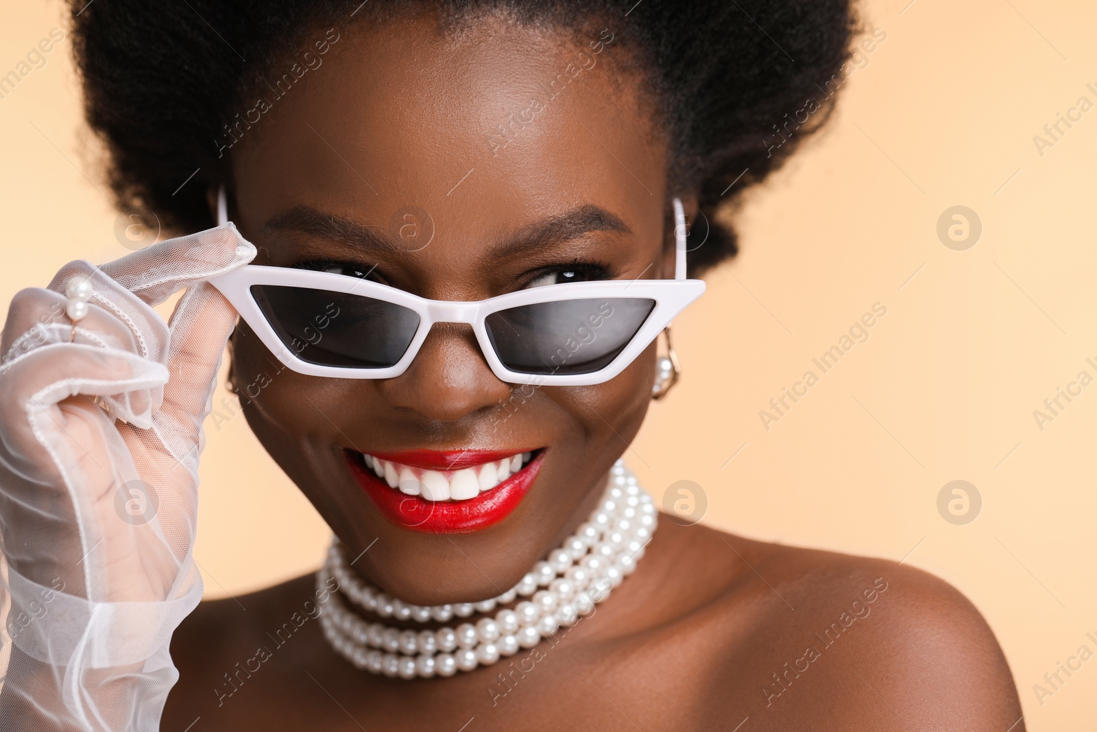 Photo of Fashionable portrait of beautiful happy woman with stylish sunglasses on beige background, closeup