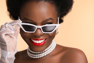 Photo of Fashionable portrait of beautiful happy woman with stylish sunglasses on beige background, closeup