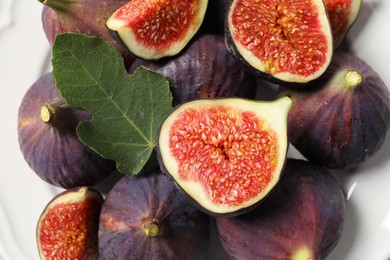Whole and cut ripe figs with leaf on plate, top view