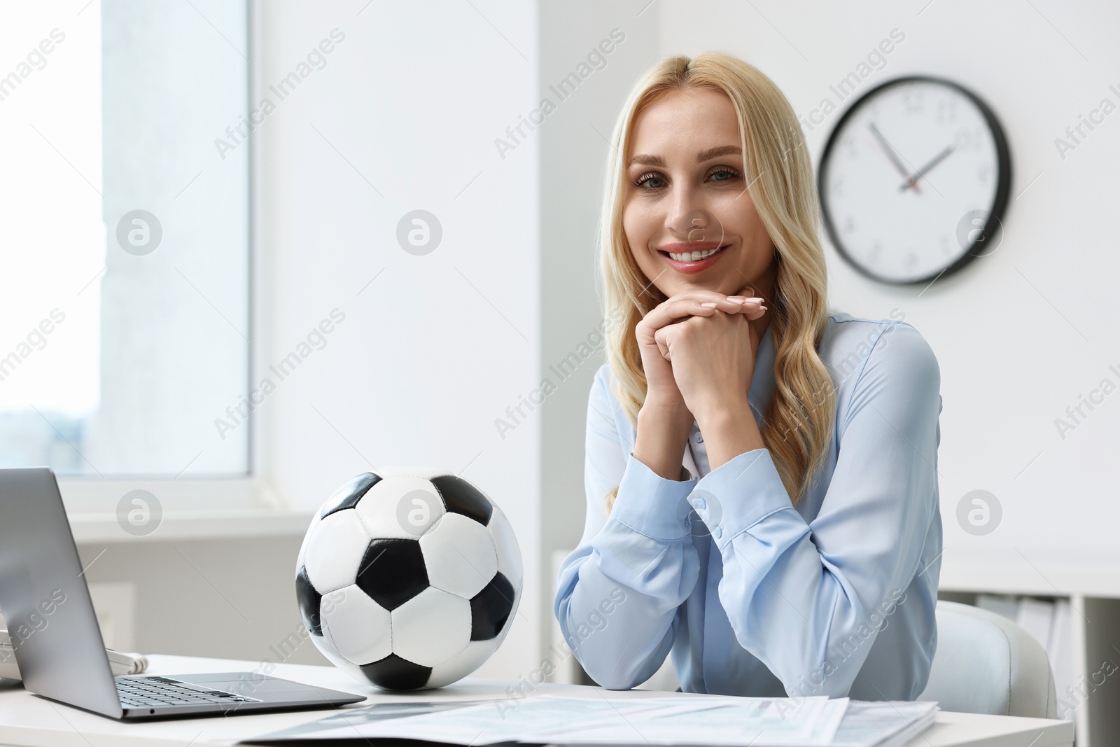 Photo of Happy woman with soccer ball at table in office