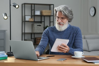 Photo of Middle aged man with laptop and notebook learning at table indoors
