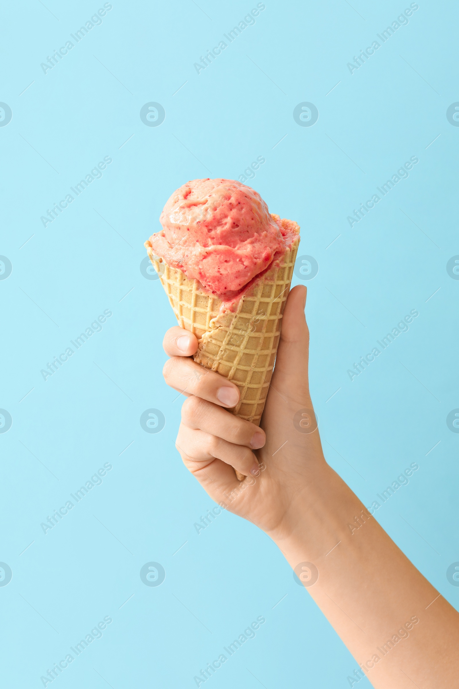 Photo of Woman holding waffle cone with delicious pink ice cream on light blue background, closeup