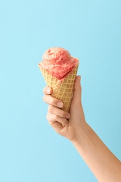 Woman holding waffle cone with delicious pink ice cream on light blue background, closeup