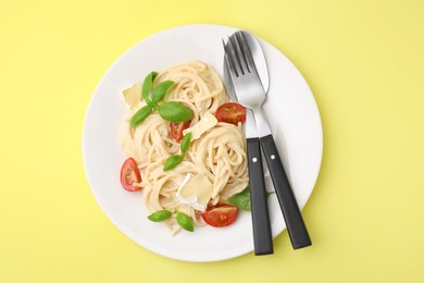Photo of Delicious pasta with brie cheese, tomatoes, basil and cutlery on yellow background, top view