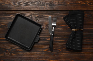 Baking dish, cutlery and towel on brown wooden table, flat lay. Cooking utensils