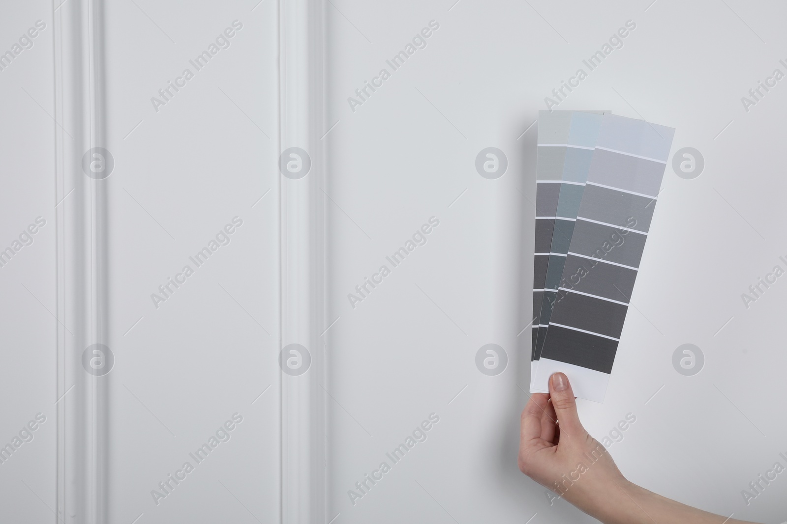 Photo of Woman with paint chips choosing color near white wall, closeup. Interior design