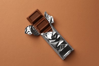 Delicious chocolate bar wrapped in foil on light brown background, top view