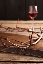 Photo of Crown of thorns and glass with wine on wooden table, selective focus