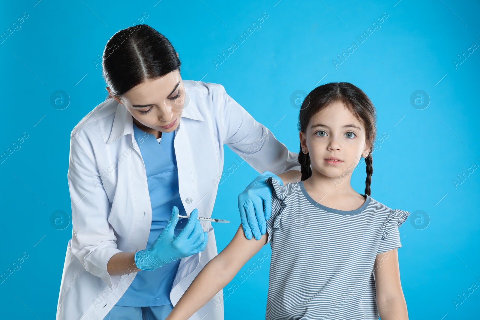 Photo of Doctor vaccinating little child on light blue background