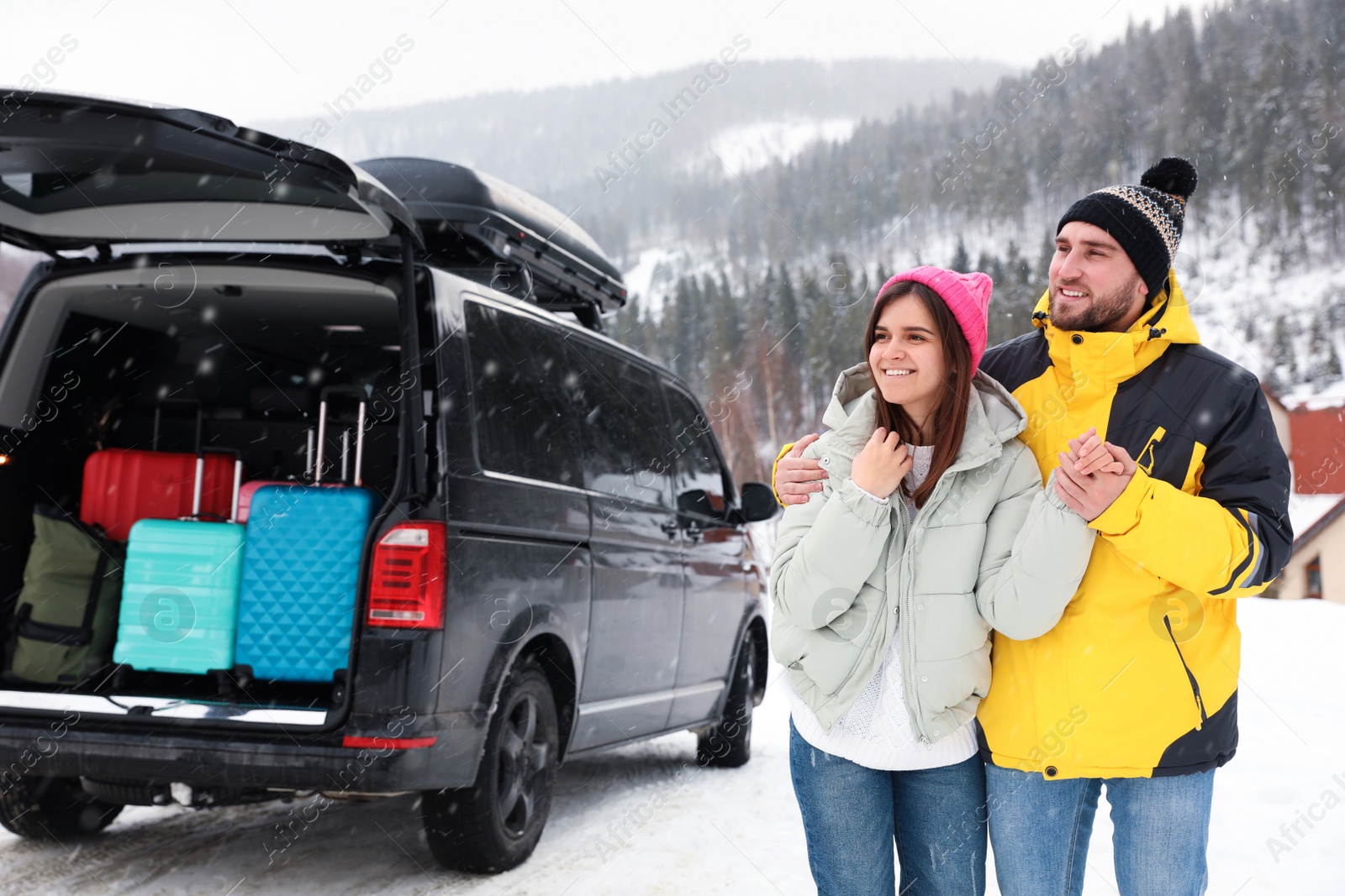 Photo of Happy couple near car with open trunk on snowy road. Winter vacation