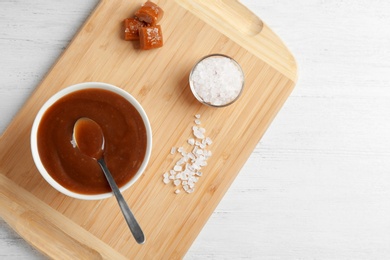 Flat lay composition with bowl of caramel sauce and salt on wooden table. Space for text