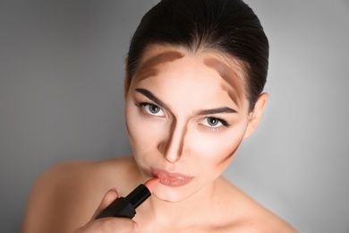 Photo of Young woman applying lipstick on grey background. Professional makeup products