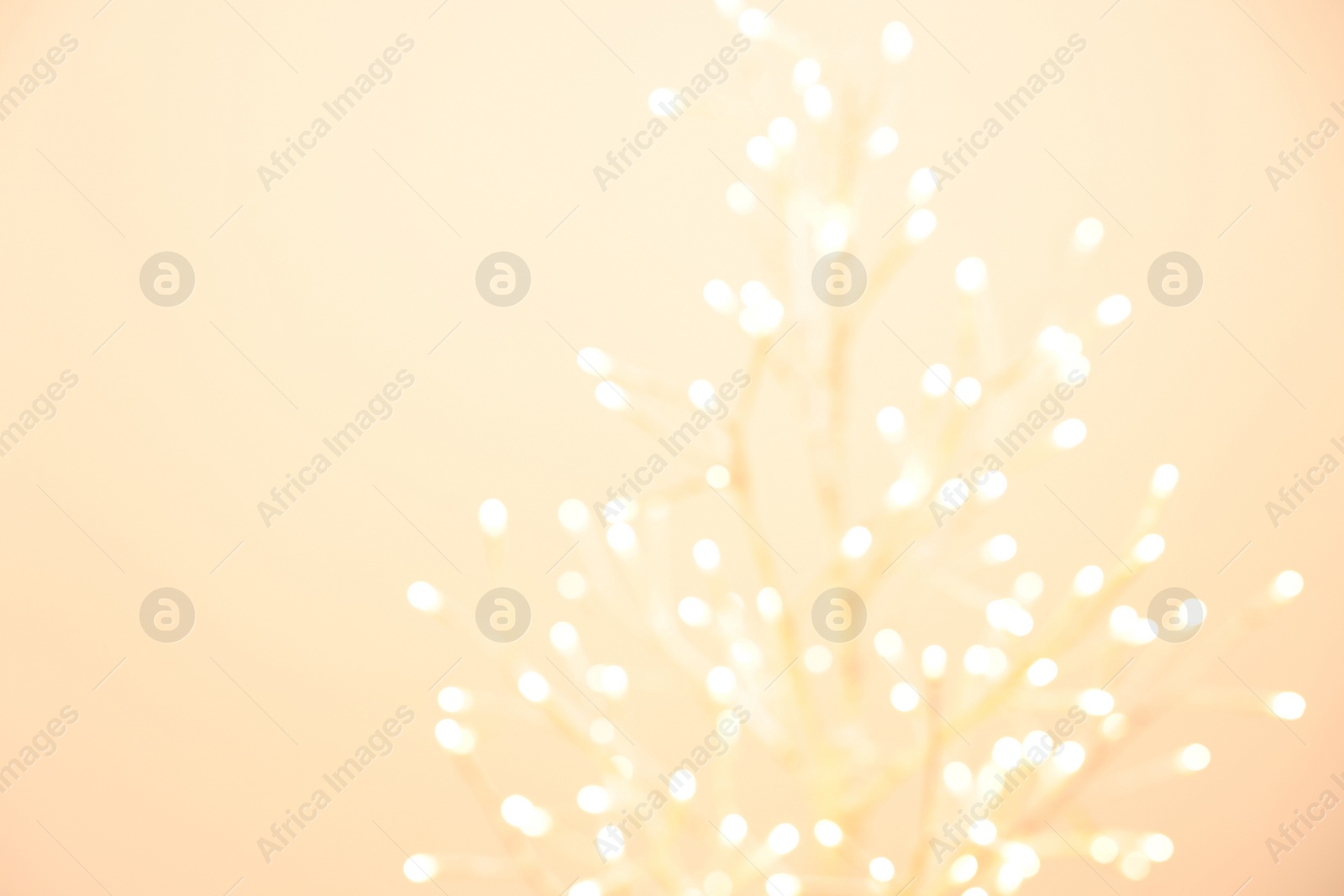 Photo of Decorative tree with lights on beige background, blurred view. Space for text