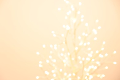 Photo of Decorative tree with lights on beige background, blurred view. Space for text