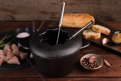 Fondue pot, pieces of raw meat, bread and spices on wooden table