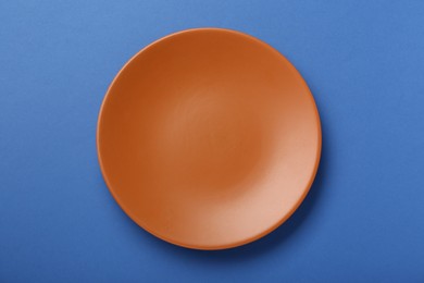 Empty orange ceramic plate on blue background, top view