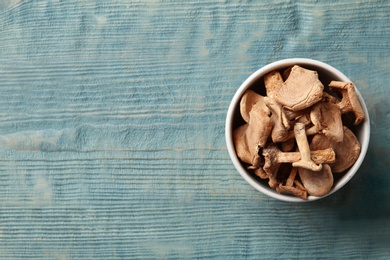 Bowl of dried mushrooms on color wooden background, top view with space for text