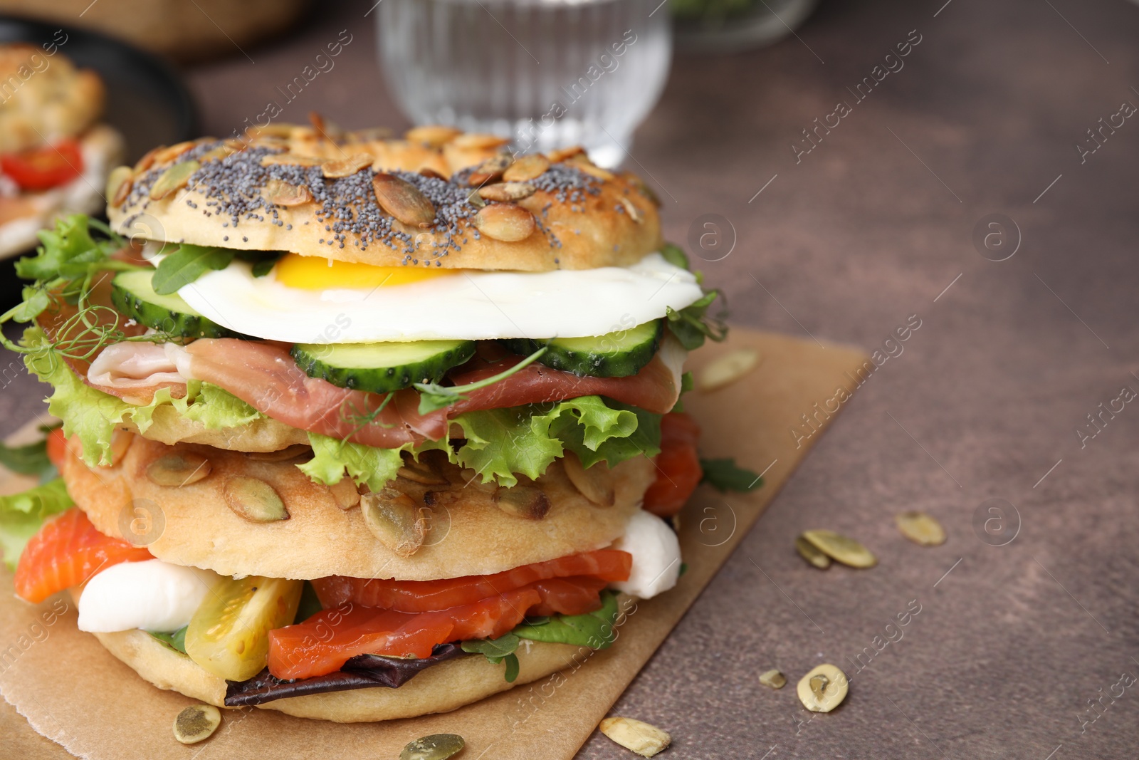 Photo of Tasty bagel with cured ham, egg, salmon and vegetables on brown table, closeup. Space for text