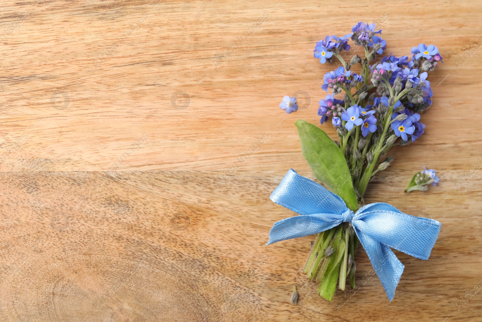 Photo of Beautiful blue forget-me-not flowers tied with ribbon on wooden table, top view. Space for text