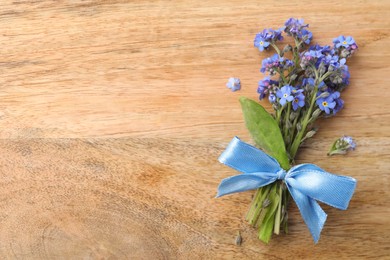 Beautiful blue forget-me-not flowers tied with ribbon on wooden table, top view. Space for text