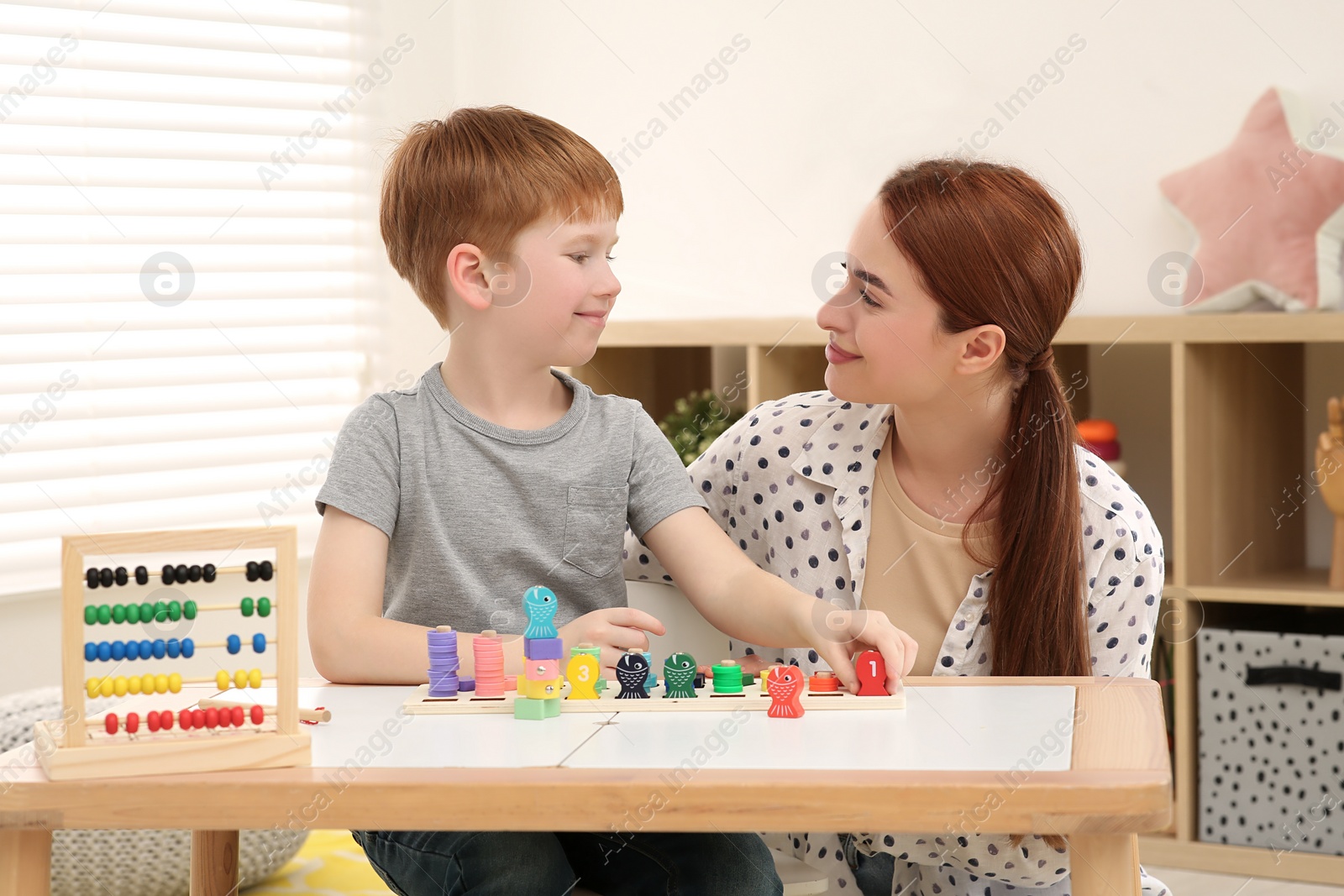 Photo of Happy mother and son playing with Educational game Fishing for Numbers at desk in room. Learning mathematics with fun