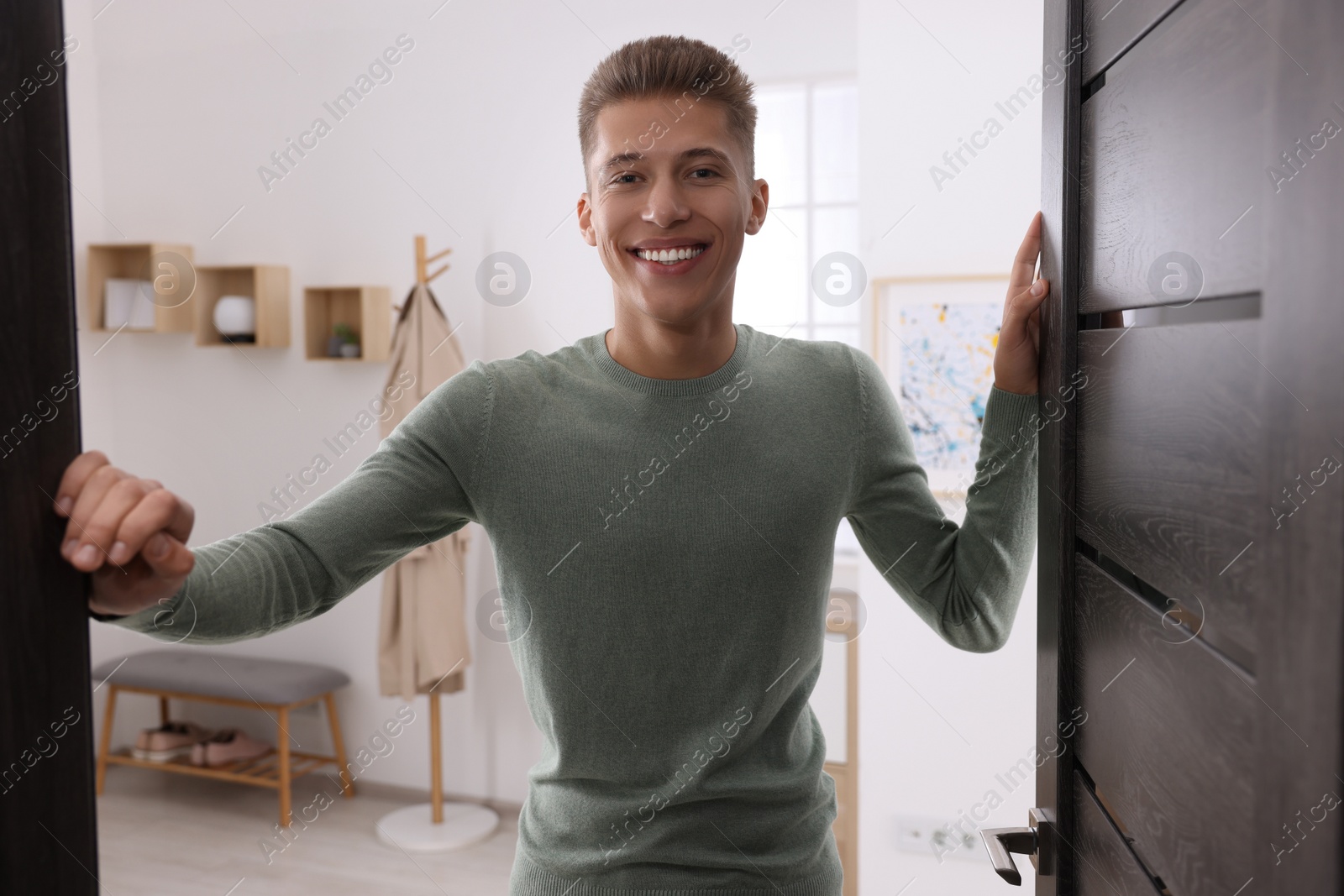 Photo of Happy man standing near door. Invitation to come indoors