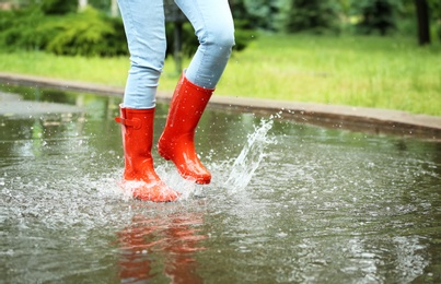 Woman with red rubber boots jumping in puddle, closeup. Rainy weather