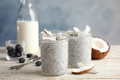 Photo of Tasty chia seed pudding with coconut in jars and ingredients on table