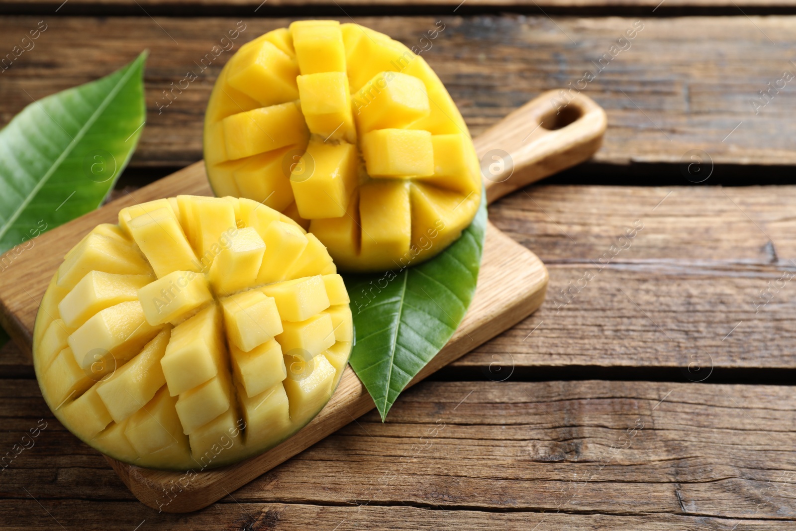 Photo of Halves of ripe mango cut into cubes on wooden table