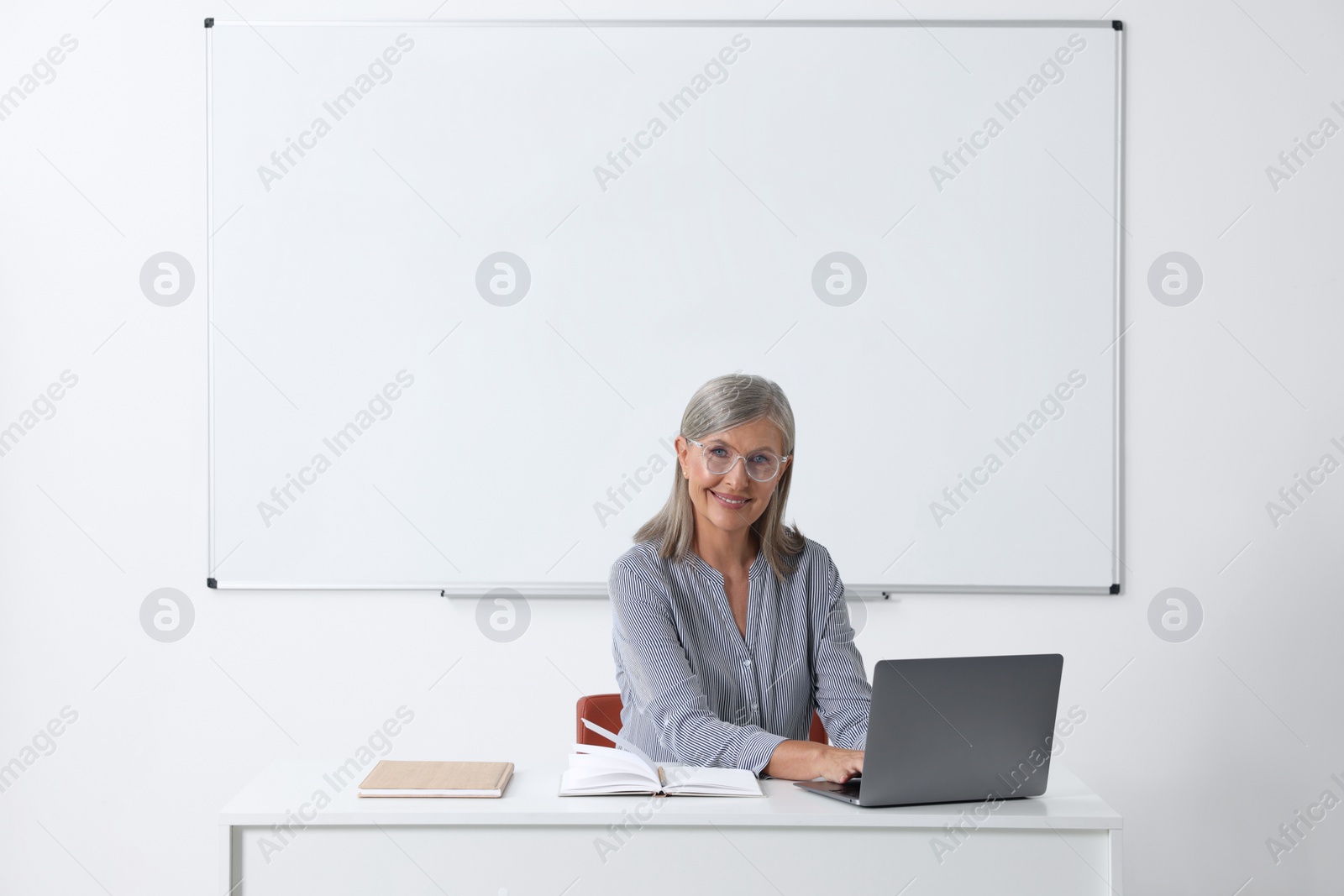 Photo of Happy professor giving lecture while using laptop at desk in classroom