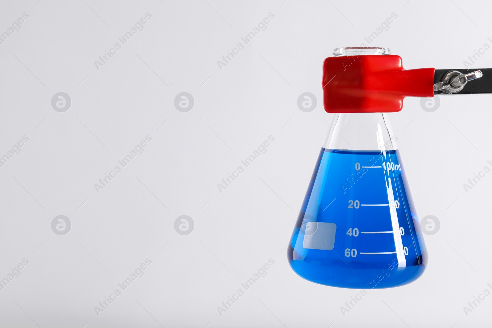 Photo of Retort stand and laboratory flask with liquid on white background, closeup. Space for text