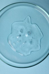 Petri dish with sample of cosmetic oil on light blue background, top view