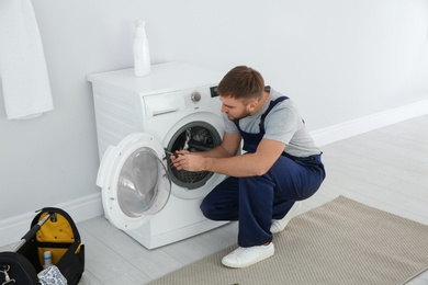 Young plumber fixing washing machine in bathroom