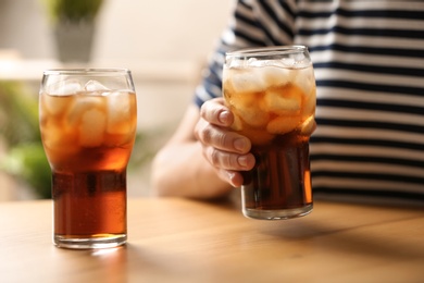 Photo of Woman holding glass of cola with ice at table, closeup