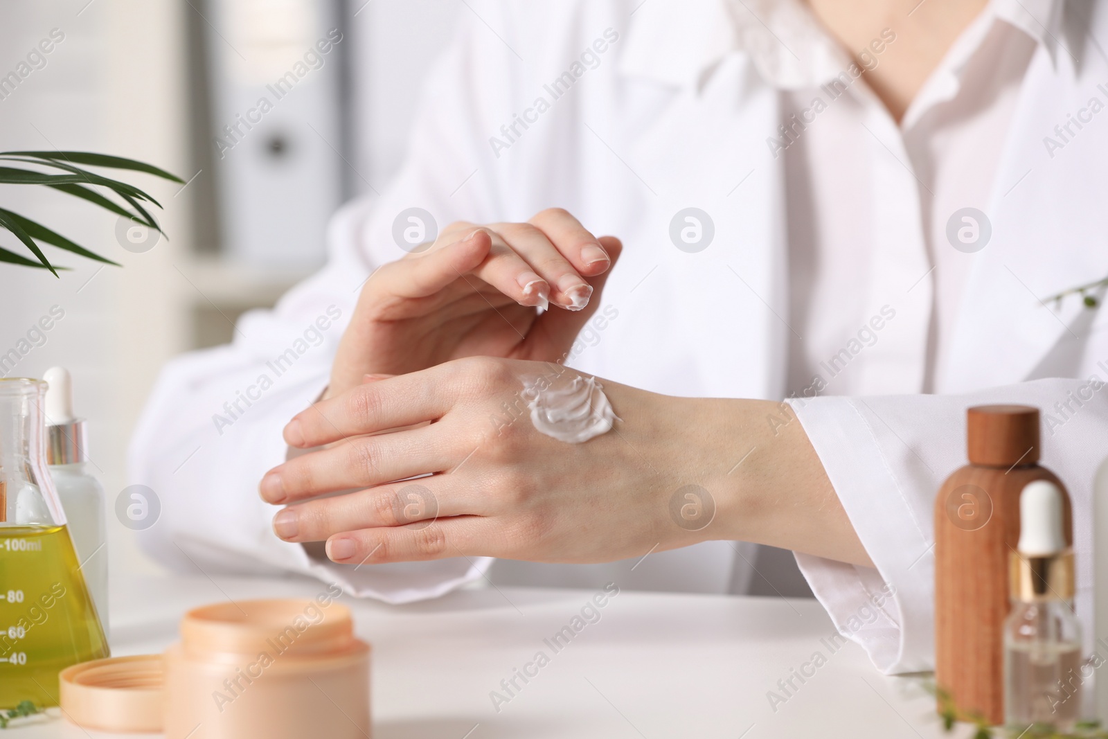 Photo of Dermatologist applying cream onto hand at white table indoors, selective focus. Testing cosmetic product