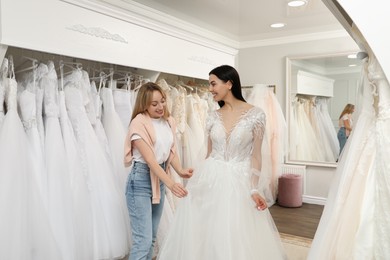 Photo of Woman helping bride wear wedding dress in boutique