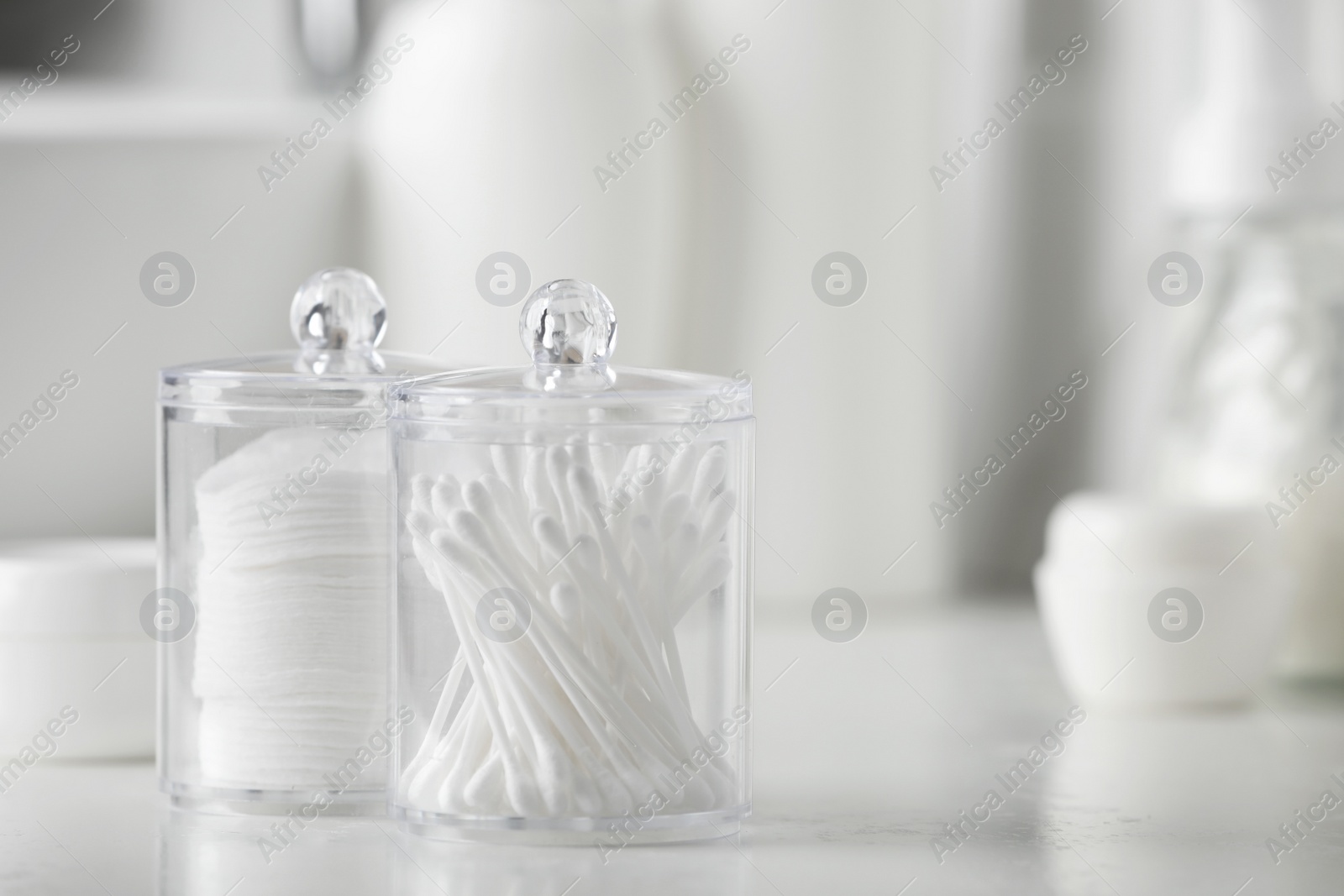 Photo of Containers with cotton swabs and pads on white countertop in bathroom, closeup. Space for text