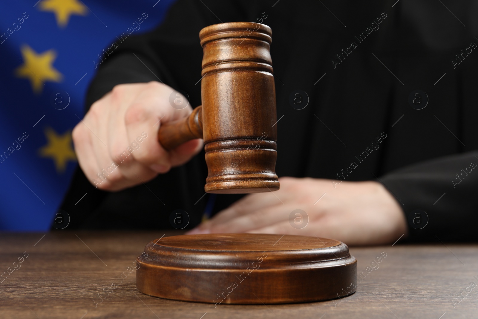 Photo of Judge with gavel at wooden table against flag of European Union, closeup